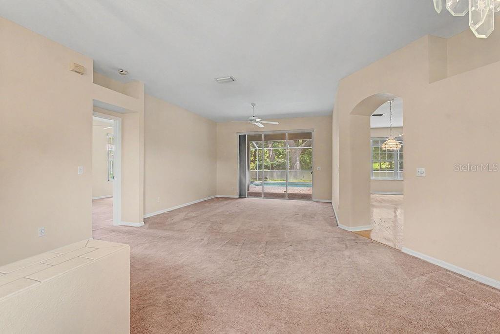 A carpeted living room features a ceiling fan, sliding glass doors, and an arched entryway — 9009 SW 194TH COURT, DUNNELLON, FL
