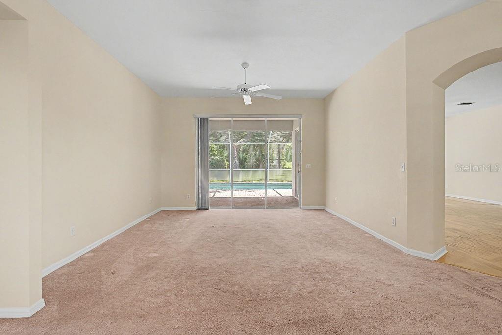 An empty room with beige carpet, a ceiling fan, and sliding doors leading to a pool — 9009 SW 194TH COURT, DUNNELLON, FL