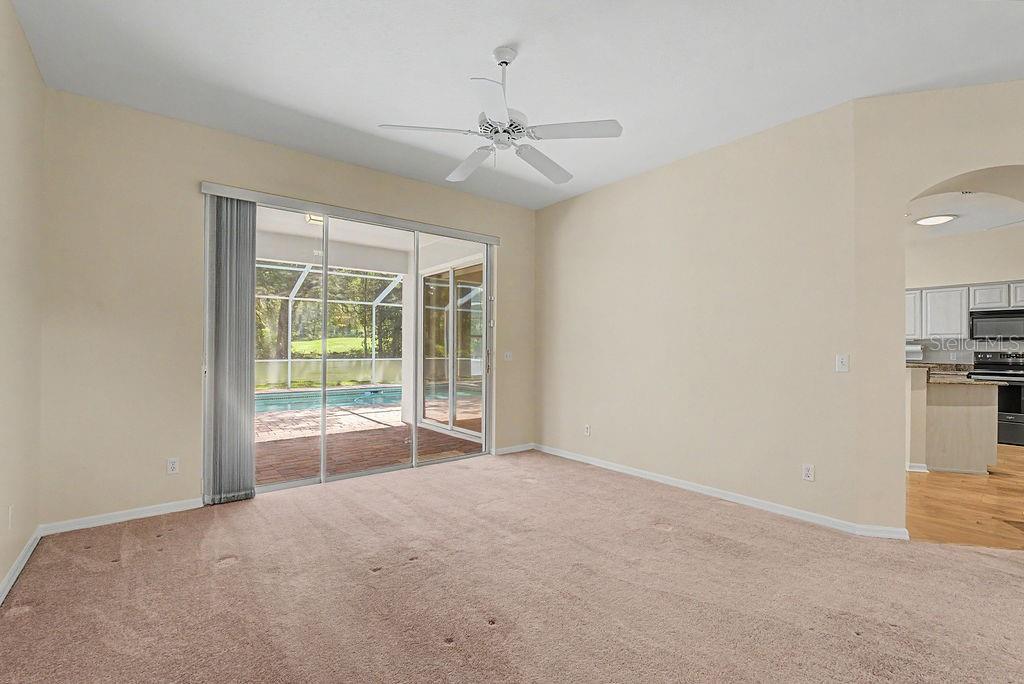 An empty carpeted room features a ceiling fan and sliding glass doors overlooking a pool — 9009 SW 194TH COURT, DUNNELLON, FL