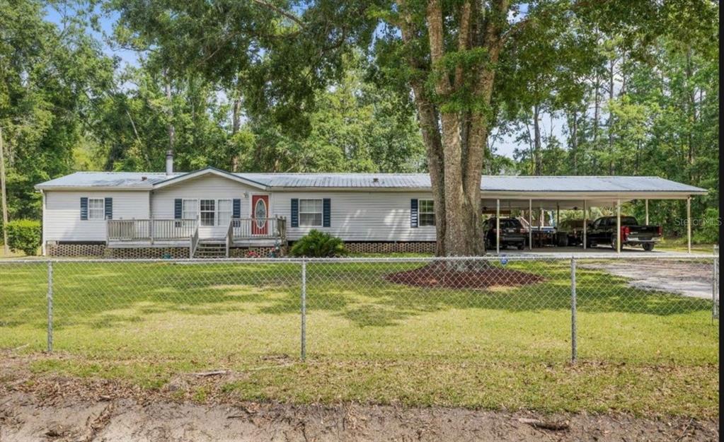 A single-story house with a metal roof, front deck, and attached carport behind a fence — 245 NW GENELL LOOP, LAKE CITY, FL