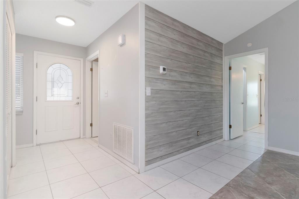 A tiled entryway features a white front door and a grey wood-plank accent wall — 303 BARSTOW COURT, SUN CITY CENTER, FL