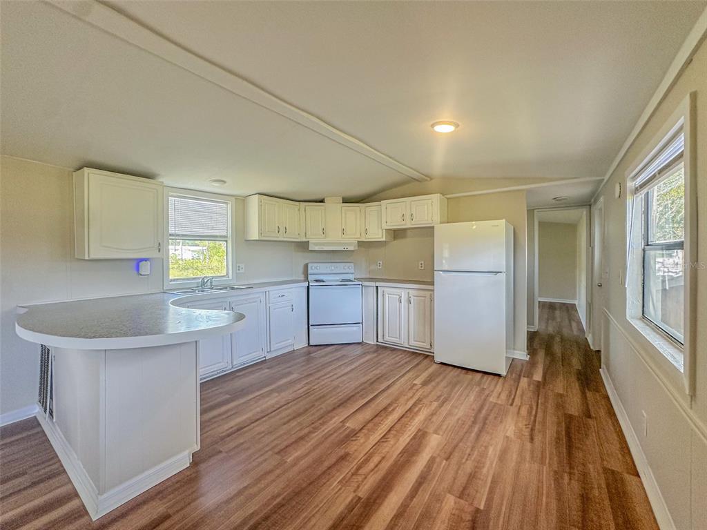 A kitchen with white cabinets, white appliances, and wood-look flooring features a curved breakfast bar — 2218 ELLIE ROAD UNIT 1, AUBURNDALE, FL