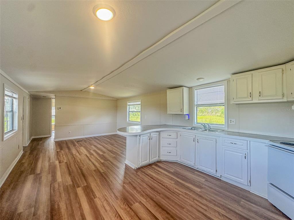 An open-concept kitchen and living area featuring white cabinets, laminate countertops, and wood-look flooring — 2218 ELLIE ROAD UNIT 1, AUBURNDALE, FL