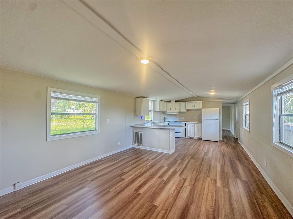 An open-concept kitchen and living area featuring light wood-look flooring and white cabinetry — 2218 ELLIE ROAD UNIT 1, AUBURNDALE, FL