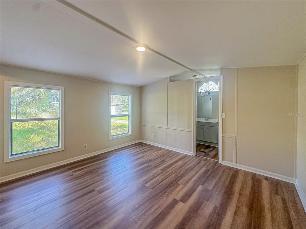 An empty room with wood-look flooring, two windows, and a doorway leading to a bathroom — 2218 ELLIE ROAD UNIT 1, AUBURNDALE, FL