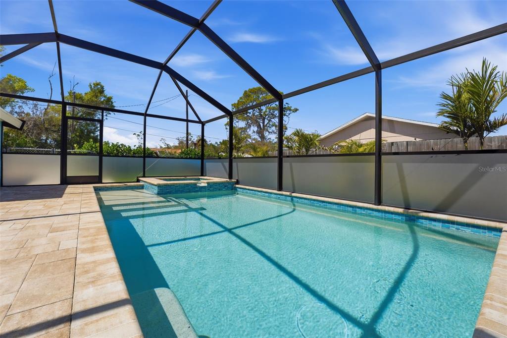 A screened-in swimming pool and attached hot tub with light-colored pavers and privacy panels — 2400 PINE COURT, NOKOMIS, FL