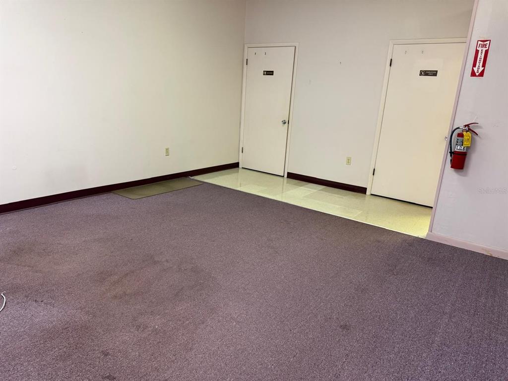An empty room with purple carpet, two white doors, and a wall-mounted fire extinguisher — 6000 STATE ROAD 544, WINTER HAVEN, FL