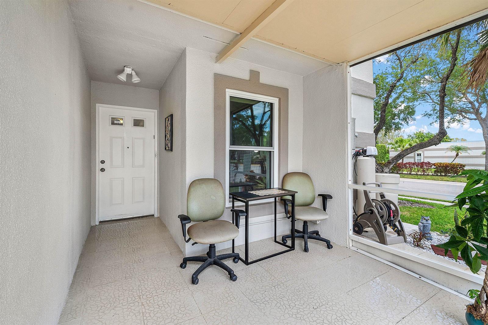 A covered porch features tiled flooring, two office chairs, a small table, and a white door — 18881 Jolson Avenue # 1, Boca Raton FL 33496, BOCA RATON, FL