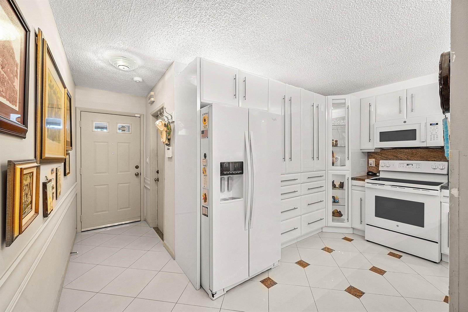 A kitchen features white cabinetry, a white refrigerator, a white stove, and light-colored tiled flooring — 18881 Jolson Avenue # 1, Boca Raton FL 33496, BOCA RATON, FL