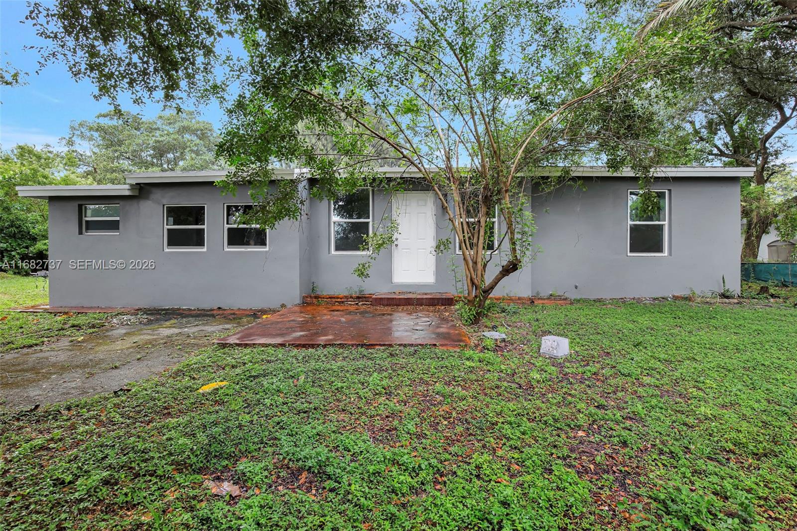 A single-story gray house with a white front door and a concrete patio area — 4381 SW 51st St, Dania Beach FL 33314, DANIA BEACH, FL