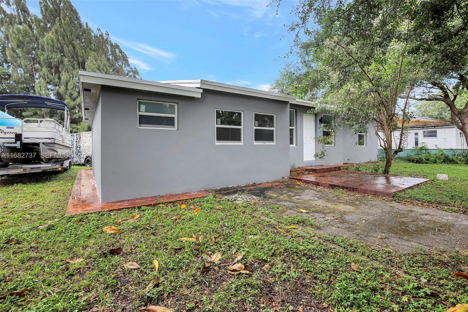 A gray, single-story house exterior features a white door, multiple windows, and a concrete patio — 4381 SW 51st St, Dania Beach FL 33314, DANIA BEACH, FL