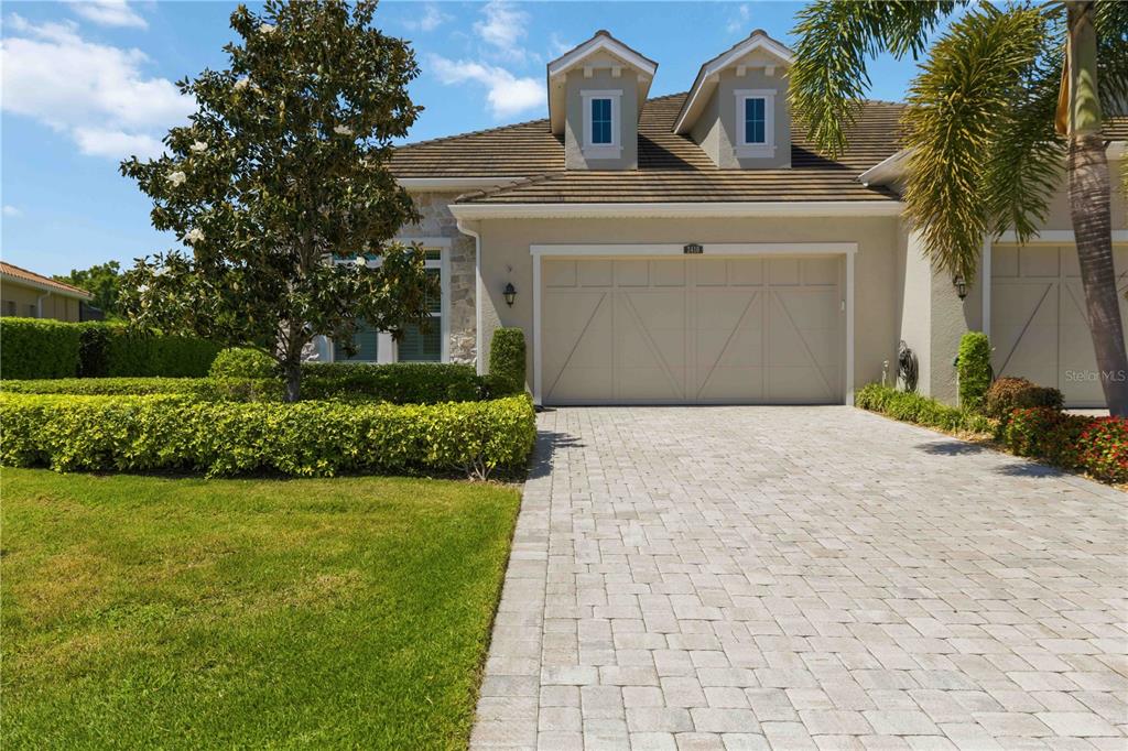 A beige house features a two-car garage, a paver driveway, and two dormer windows — 2410 STARWOOD COURT, BRADENTON, FL