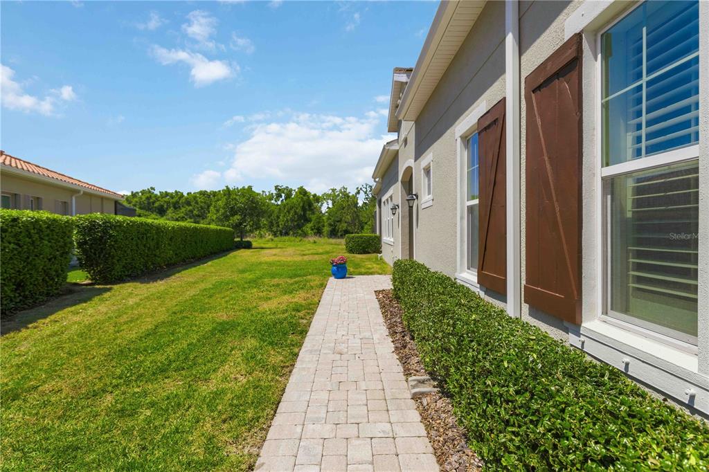 A paved walkway runs alongside a house exterior with brown shutters and a manicured hedge — 2410 STARWOOD COURT, BRADENTON, FL