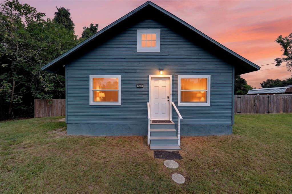 A blue single-story house with a white front door and steps at sunset — 705 NW 64TH PLACE, OCALA, FL