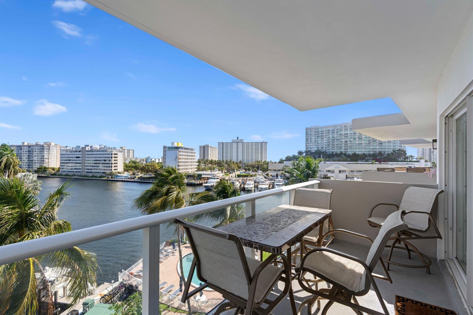 A balcony with patio furniture overlooks a waterway, swimming pool, and city skyline — 140 NE 28th # 604, Pompano Beach FL 33062, POMPANO BEACH, FL