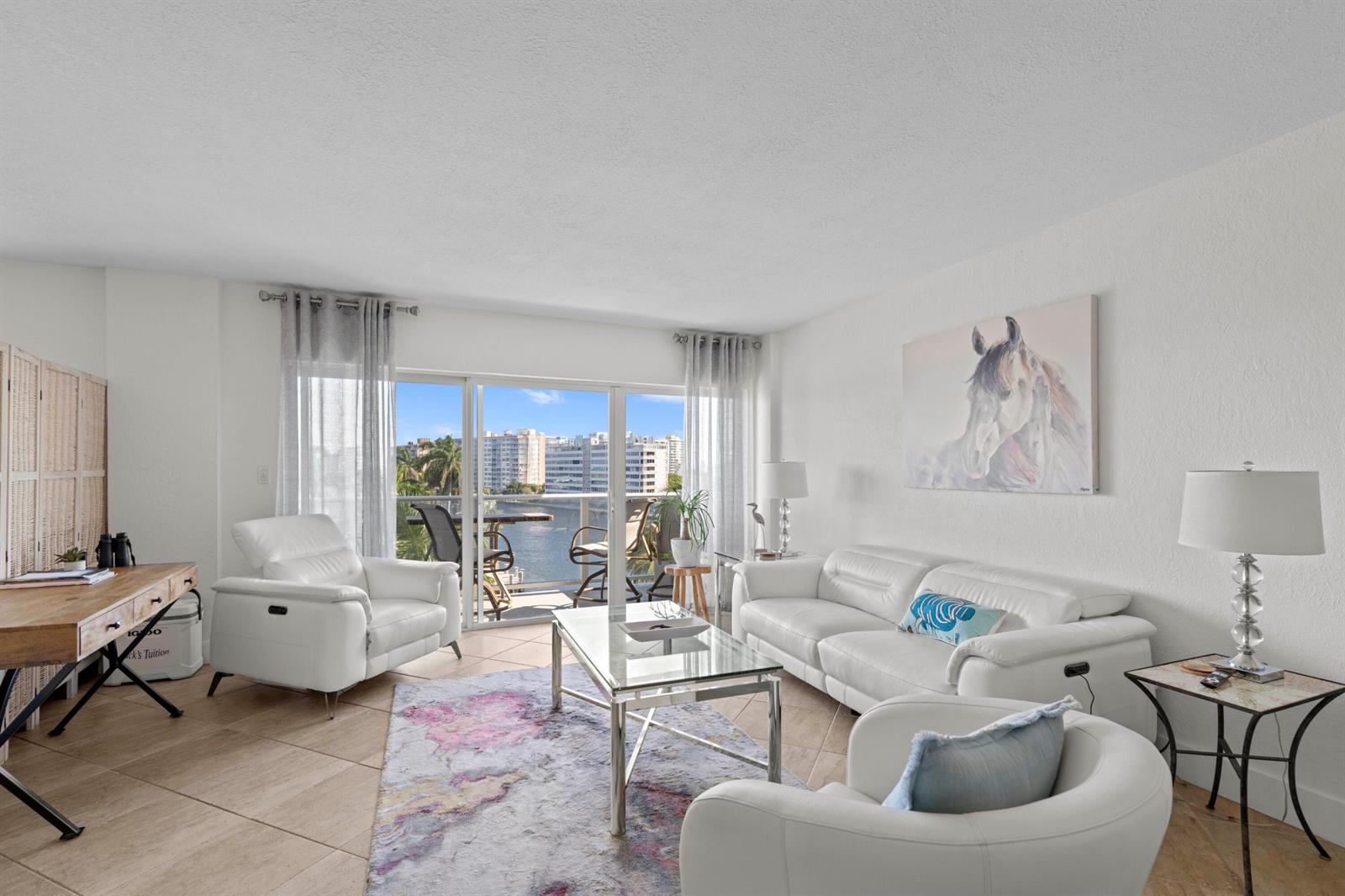 A bright living room features white leather furniture, a glass coffee table, and balcony views — 140 NE 28th # 604, Pompano Beach FL 33062, POMPANO BEACH, FL