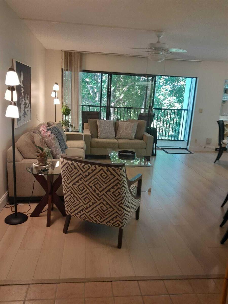 A living room features light wood flooring, a patterned armchair, and a sliding glass door — 1605 S Us Highway 1 # C302, Jupiter FL 33477, JUPITER, FL