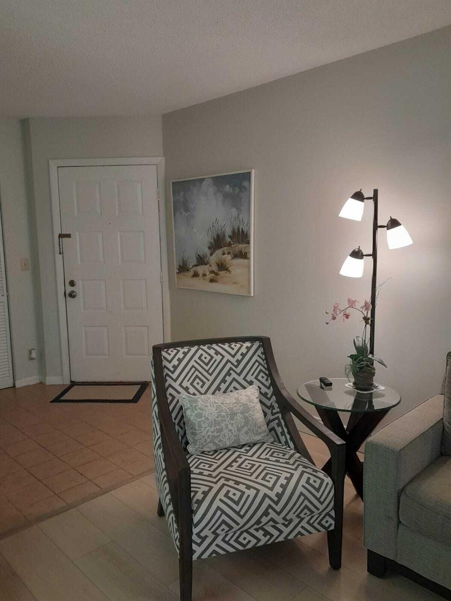 A patterned armchair sits next to a glass side table and floor lamp in a foyer — 1605 S Us Highway 1 # C302, Jupiter FL 33477, JUPITER, FL