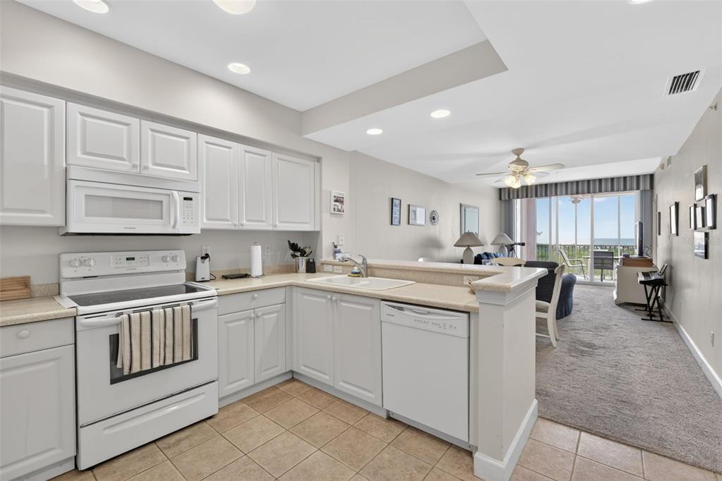 A kitchen with white cabinets and appliances opens to a carpeted living area with balcony access — 3191 MATECUMBE KEY ROAD UNIT 304, PUNTA GORDA, FL