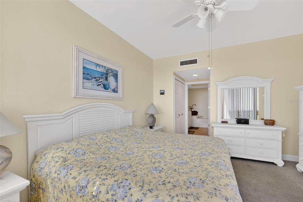 A bedroom features a white headboard, floral bedding, a white dresser with a mirror, and carpet — 3191 MATECUMBE KEY ROAD UNIT 304, PUNTA GORDA, FL