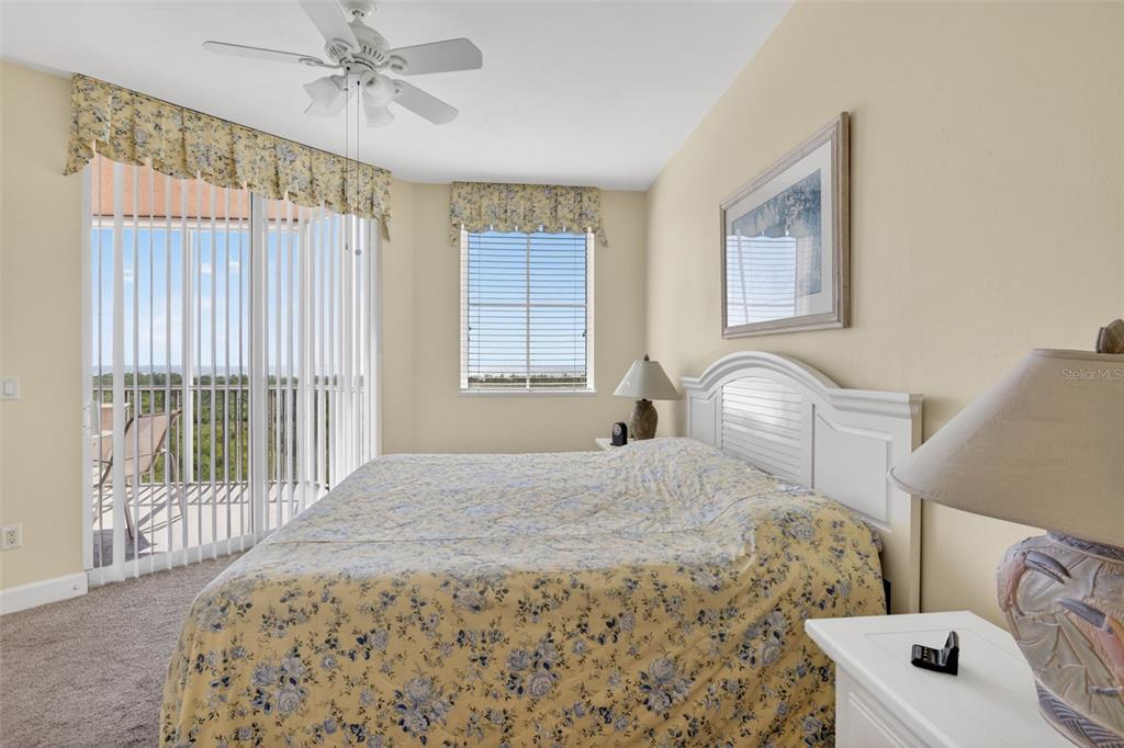 A bedroom features a bed with floral bedding, a ceiling fan, and a balcony view — 3191 MATECUMBE KEY ROAD UNIT 304, PUNTA GORDA, FL