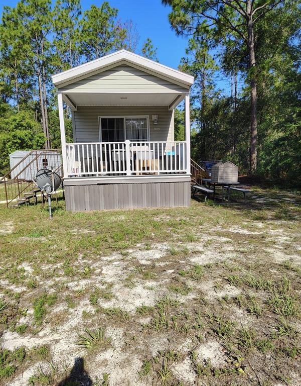 A light-colored mobile home with a front porch sits on a sandy, grassy lot — 5840 NW 11TH AVENUE, BELL, FL