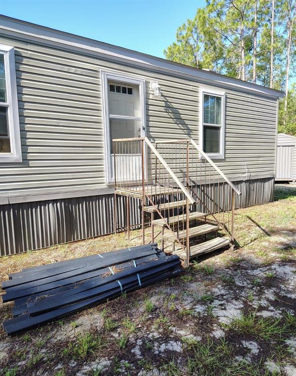 The exterior of a manufactured home features light siding, a metal staircase, and stacked wooden planks — 5840 NW 11TH AVENUE, BELL, FL