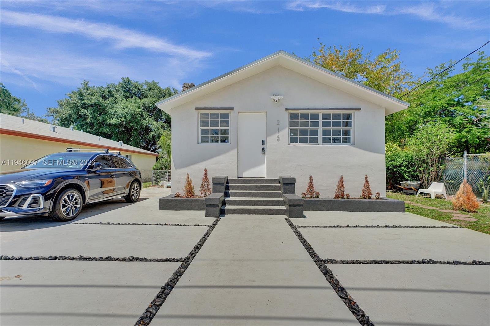 A white single-story house with a concrete driveway and a central staircase leading to the entrance — 213 NW 34th Ter, Miami FL 33127, MIAMI, FL