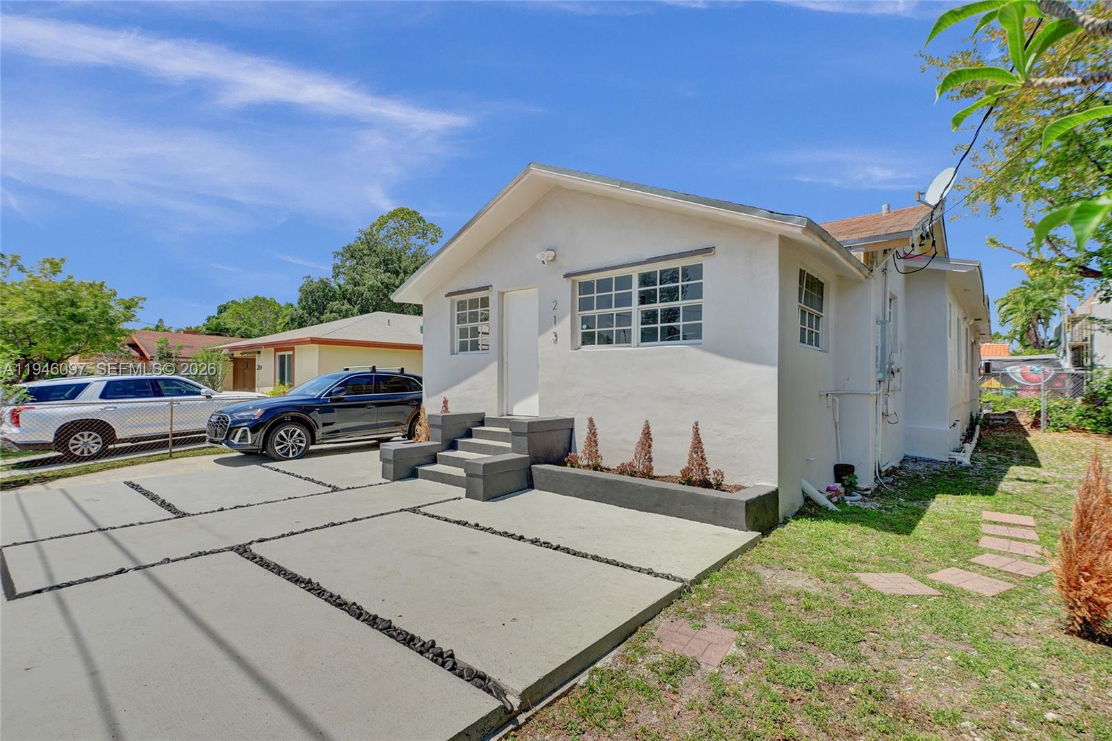 A white single-story house features a concrete driveway, gray steps, and a small front garden — 213 NW 34th Ter, Miami FL 33127, MIAMI, FL