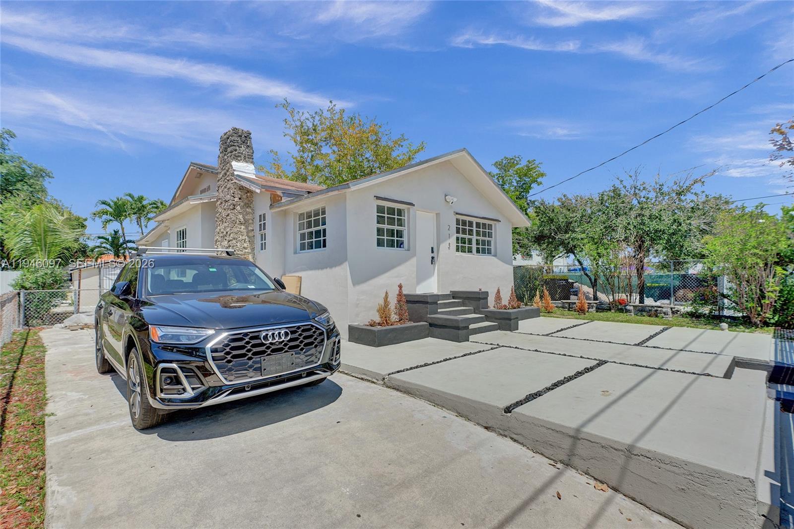 A single-story white house with a stone chimney and a concrete driveway featuring an Audi — 213 NW 34th Ter, Miami FL 33127, MIAMI, FL