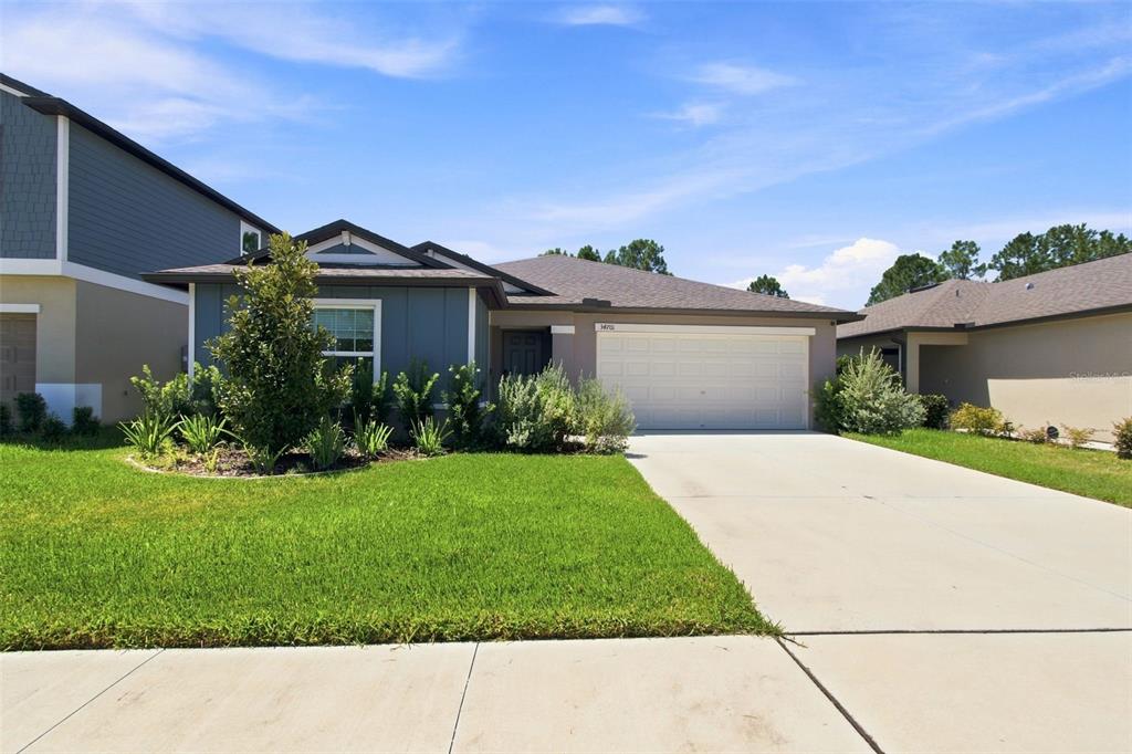A single-story house with a blue exterior, a two-car garage, and a front lawn — 34701 RAINVILLE LOOP, ZEPHYRHILLS, FL