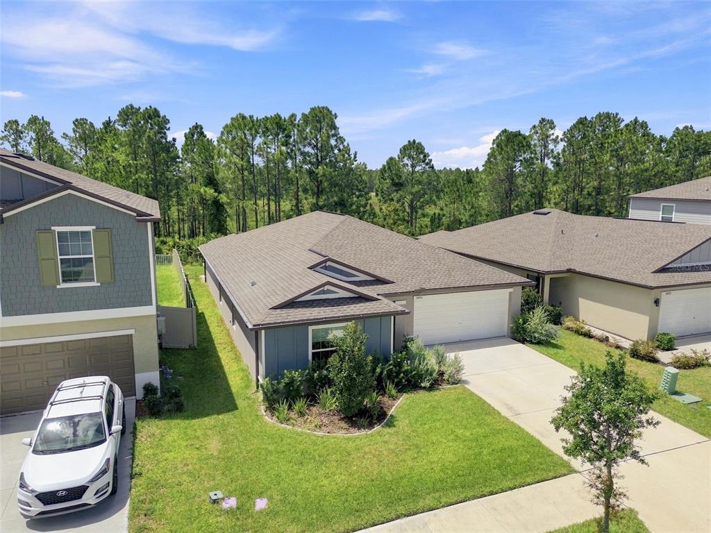 An aerial view shows a single-story house with a two-car garage and a grassy yard — 34701 RAINVILLE LOOP, ZEPHYRHILLS, FL