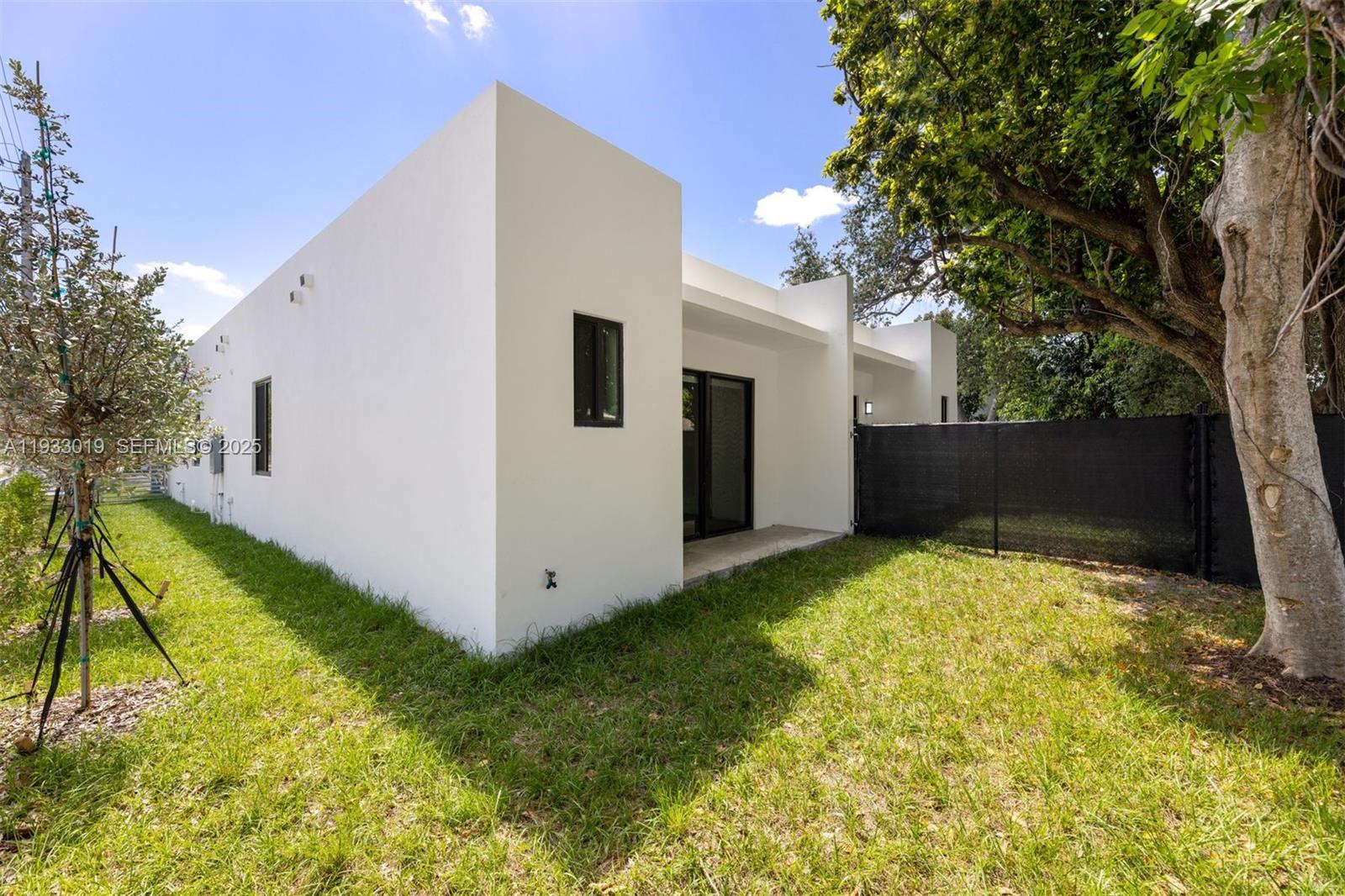 A white modern house exterior features a small backyard, a black fence, and a tree — 6852-6850 NW 4th AVE, Miami FL 33150, MIAMI, FL