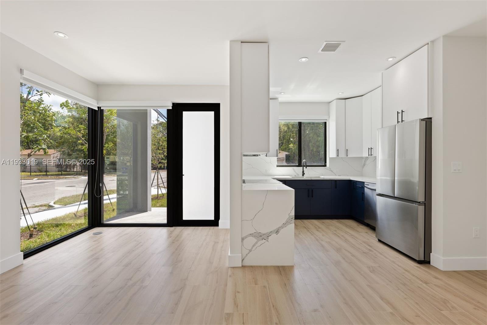 A modern kitchen features white upper cabinets, navy lower cabinets, and a marble-patterned waterfall island — 6852-6850 NW 4th AVE, Miami FL 33150, MIAMI, FL