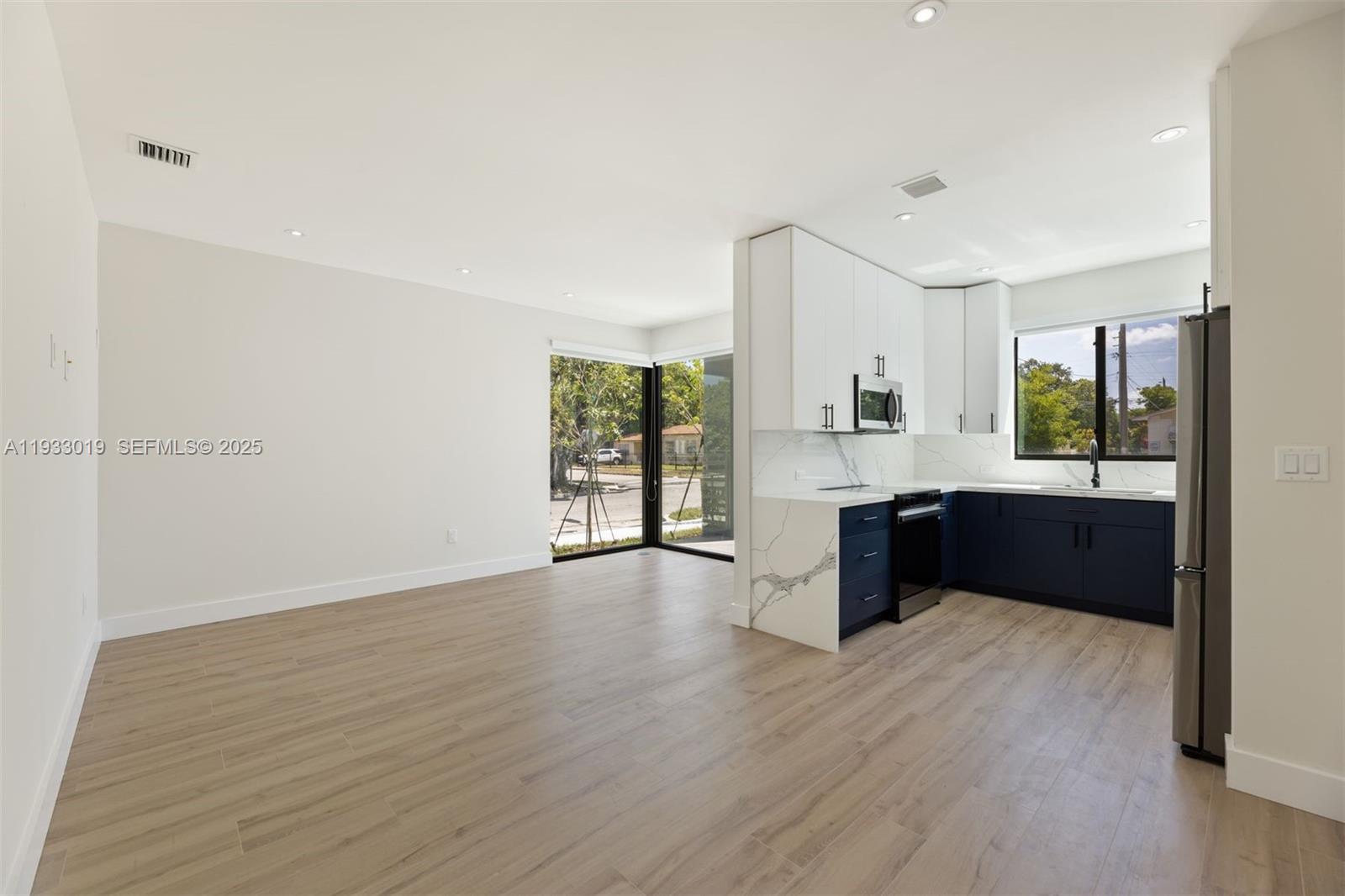 A modern kitchen with blue and white cabinetry opens into a spacious living area — 6852-6850 NW 4th AVE, Miami FL 33150, MIAMI, FL