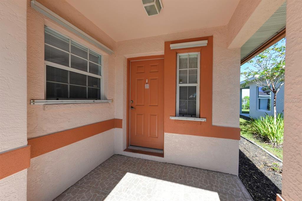 A covered entryway features a tiled floor, a peach-colored door, and orange accent trim — 483 WINWOOD COURT, PORT CHARLOTTE, FL