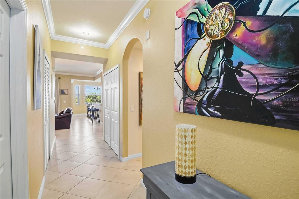 A hallway with tiled floors leads toward a living area featuring a large abstract painting — 7019 RIVER HAMMOCK DRIVE UNIT 202, BRADENTON, FL
