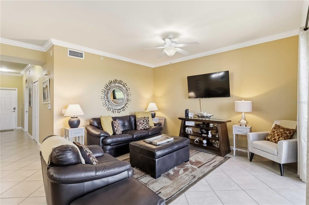 A living room features dark leather furniture, a television, a ceiling fan, and tile flooring — 7019 RIVER HAMMOCK DRIVE UNIT 202, BRADENTON, FL