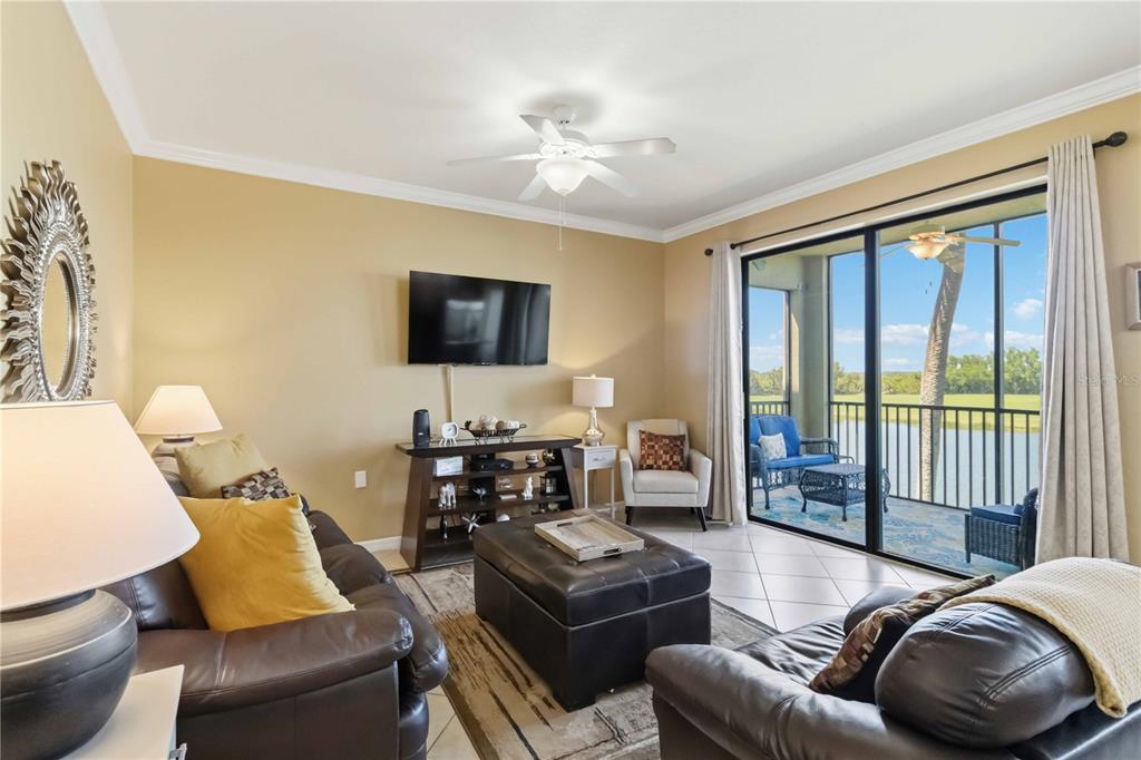 A living room features leather sofas, a television, and sliding glass doors opening to a balcony — 7019 RIVER HAMMOCK DRIVE UNIT 202, BRADENTON, FL