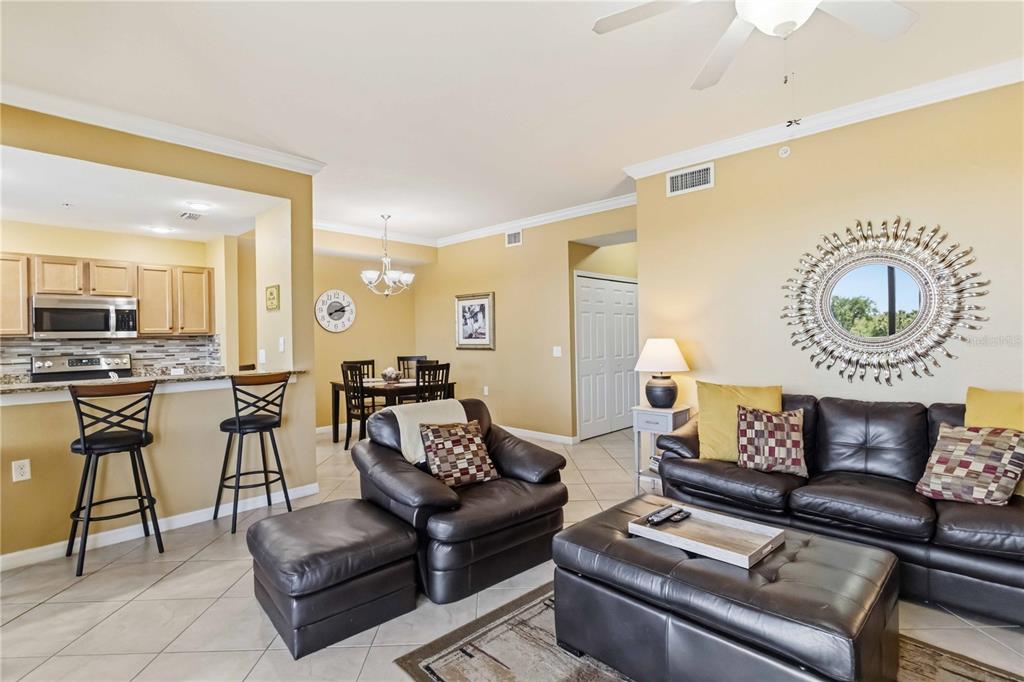 A living room with leather furniture and a mirror opens to a kitchen and dining area — 7019 RIVER HAMMOCK DRIVE UNIT 202, BRADENTON, FL
