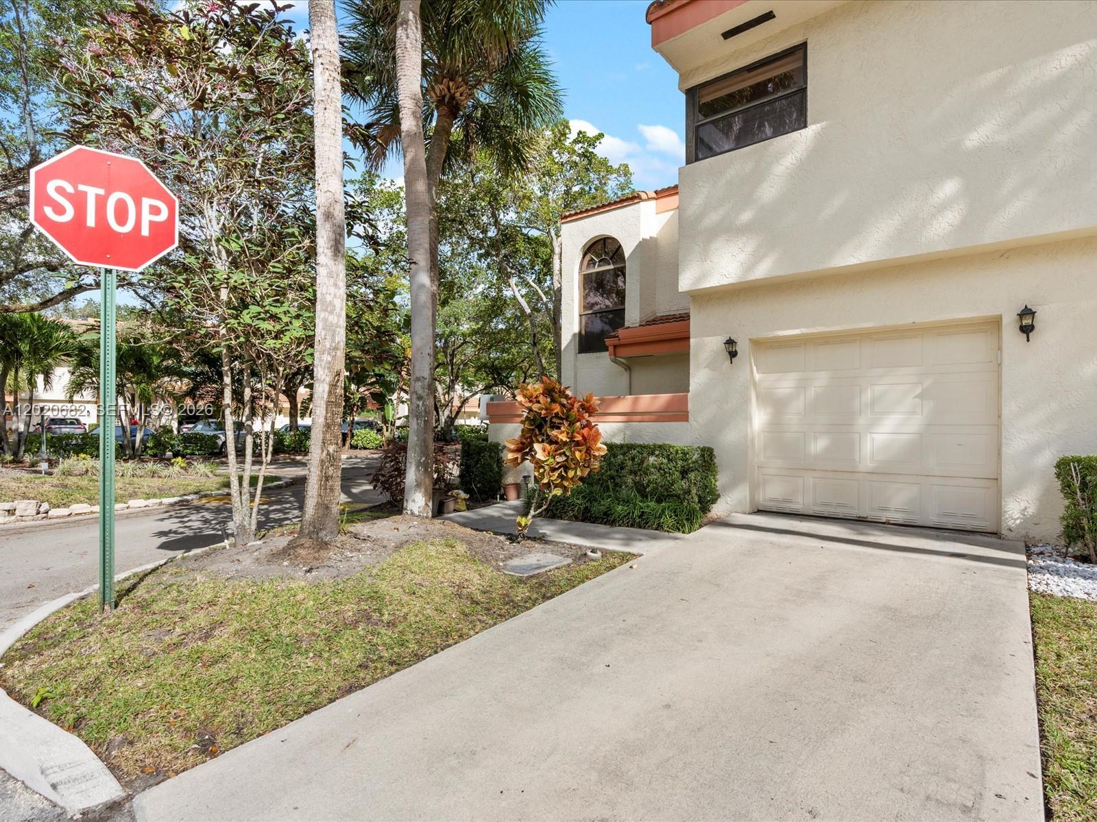 A concrete driveway leads to a garage attached to a two-story stucco home — 3400 Emerald Oaks Dr # 801, Hollywood FL 33021, HOLLYWOOD, FL