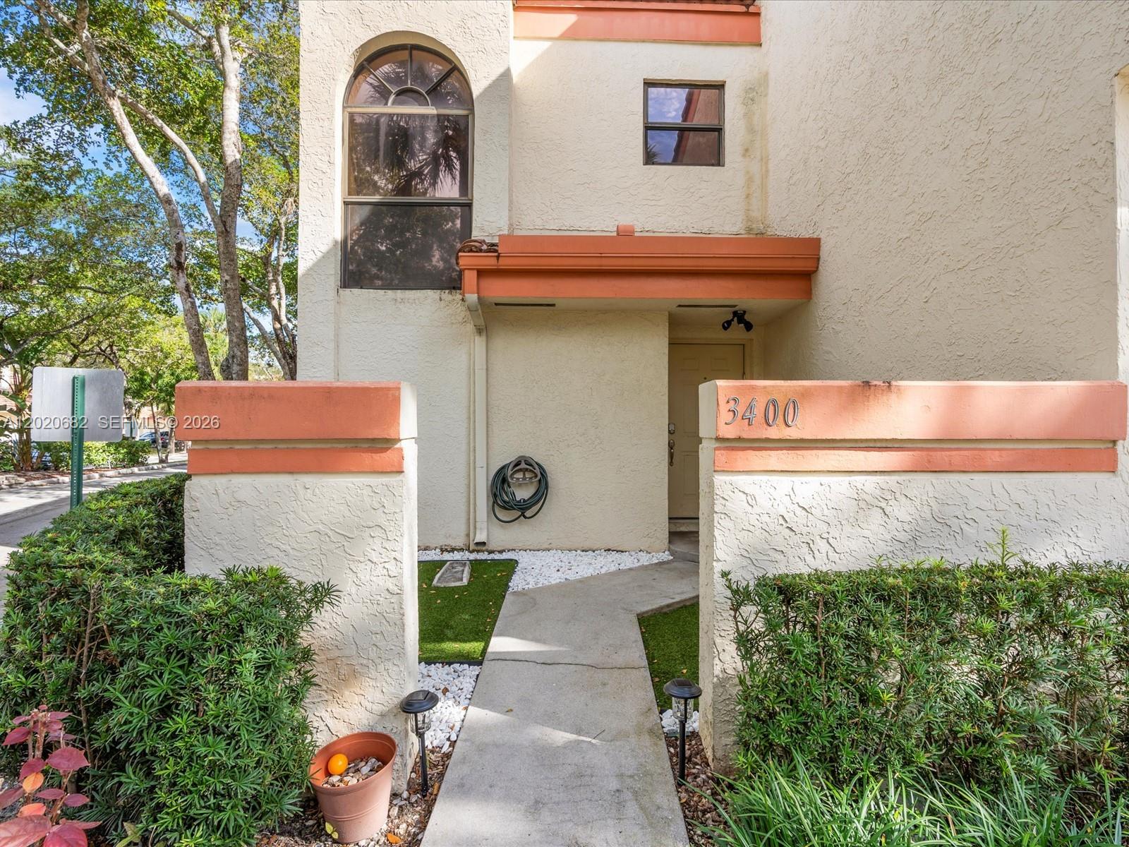 A concrete walkway leads to the entrance of a stucco townhouse with orange trim — 3400 Emerald Oaks Dr # 801, Hollywood FL 33021, HOLLYWOOD, FL