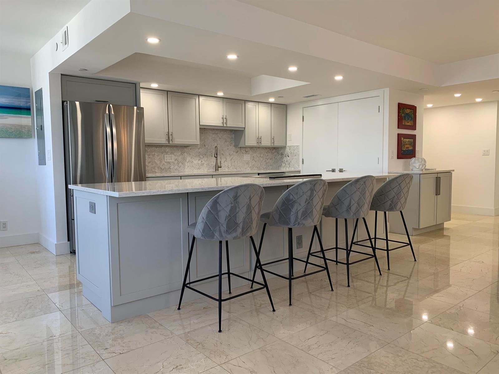 A modern kitchen features light gray cabinetry, a marble-topped island, and four velvet bar stools — 3115 S Ocean Boulevard # 1002, Highland Beach FL 33487, HIGHLAND BEACH, FL