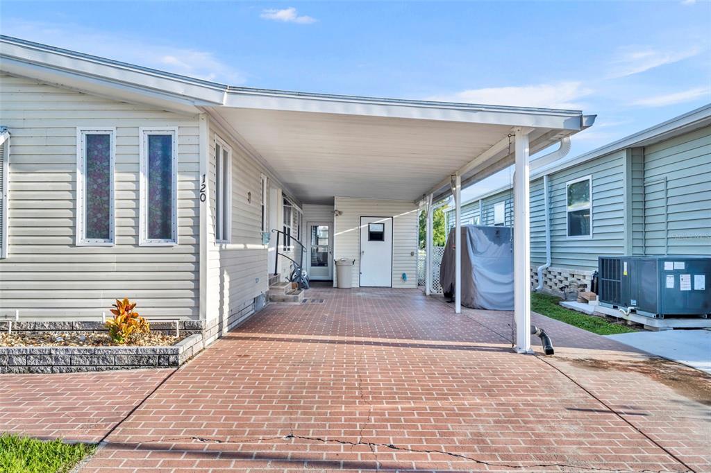 A paved carport sits between two light-colored manufactured homes under a bright blue sky — 120 VICTORIA DRIVE, HAINES CITY, FL