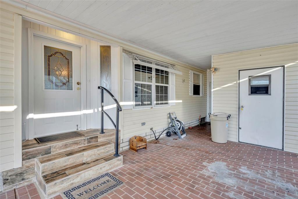 A covered brick patio leads to a front door with steps and a side entrance — 120 VICTORIA DRIVE, HAINES CITY, FL