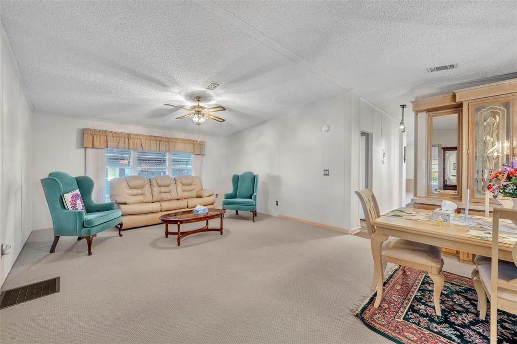 A living and dining area features beige carpeting, white walls, and a ceiling fan — 120 VICTORIA DRIVE, HAINES CITY, FL