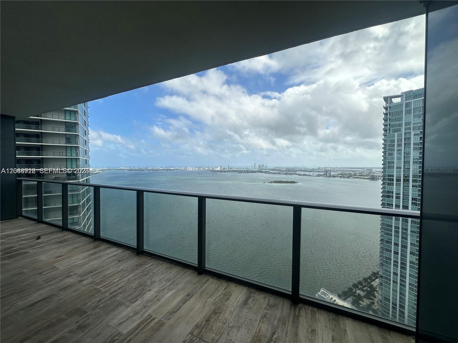 A high-rise balcony with wood-look tile flooring overlooks a bay between two glass skyscrapers — 650 NE 32nd St # 4205, Miami FL 33137, MIAMI, FL