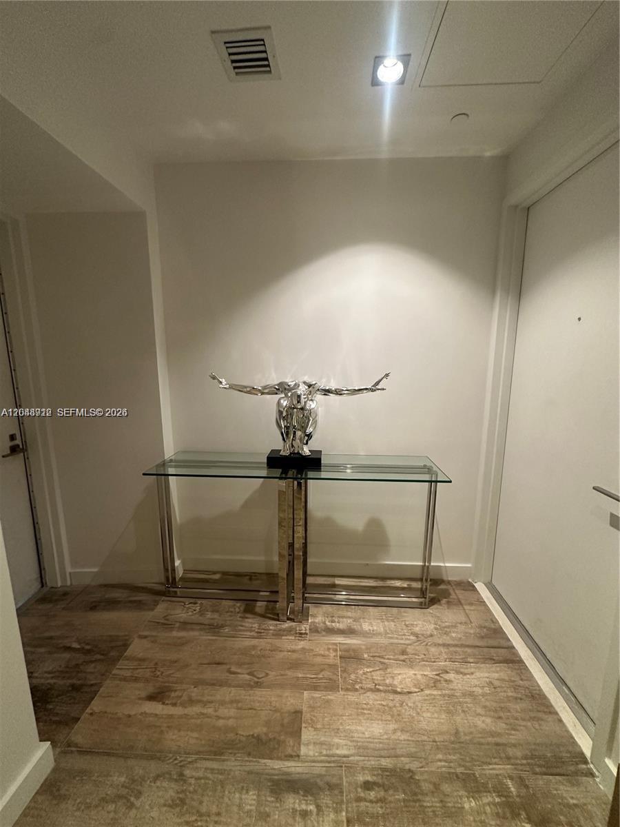A modern entryway features a glass console table, a metallic sculpture, and wood-look tile flooring — 650 NE 32nd St # 4205, Miami FL 33137, MIAMI, FL