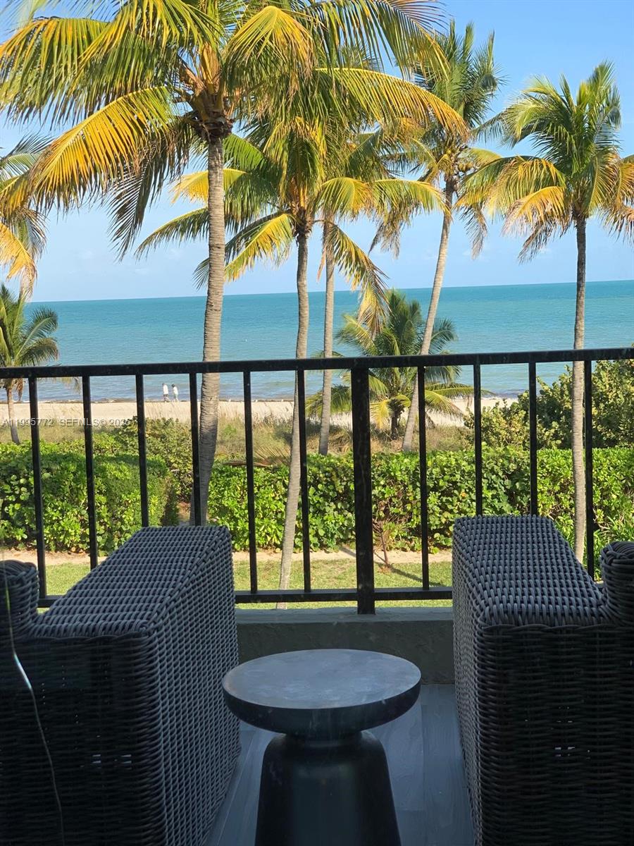 A balcony with two wicker chairs and a small table overlooks a beach and ocean — 201 Crandon Blvd # 175, Key Biscayne FL 33149, KEY BISCAYNE, FL