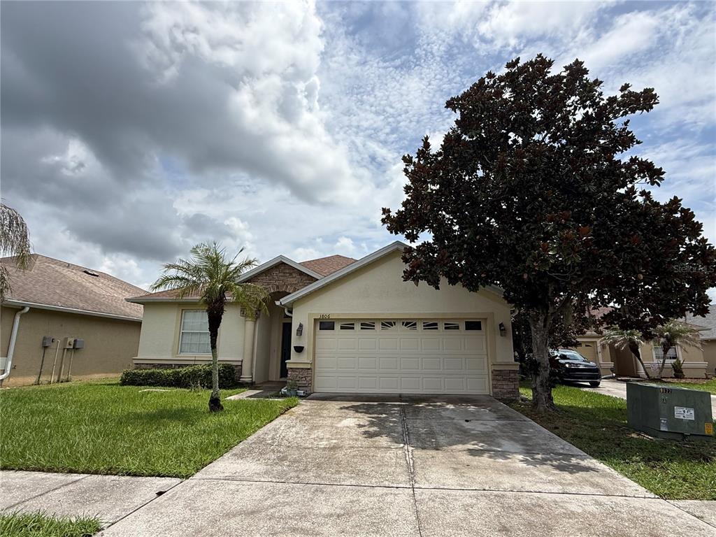 A single-story house with a two-car garage, stone accents, and a large tree in front — 3806 WASHBURN PLACE, WESLEY CHAPEL, FL